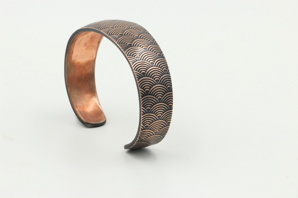 Embossed copper cuff bracelet with a repeating wave "Seigaiha," pattern.